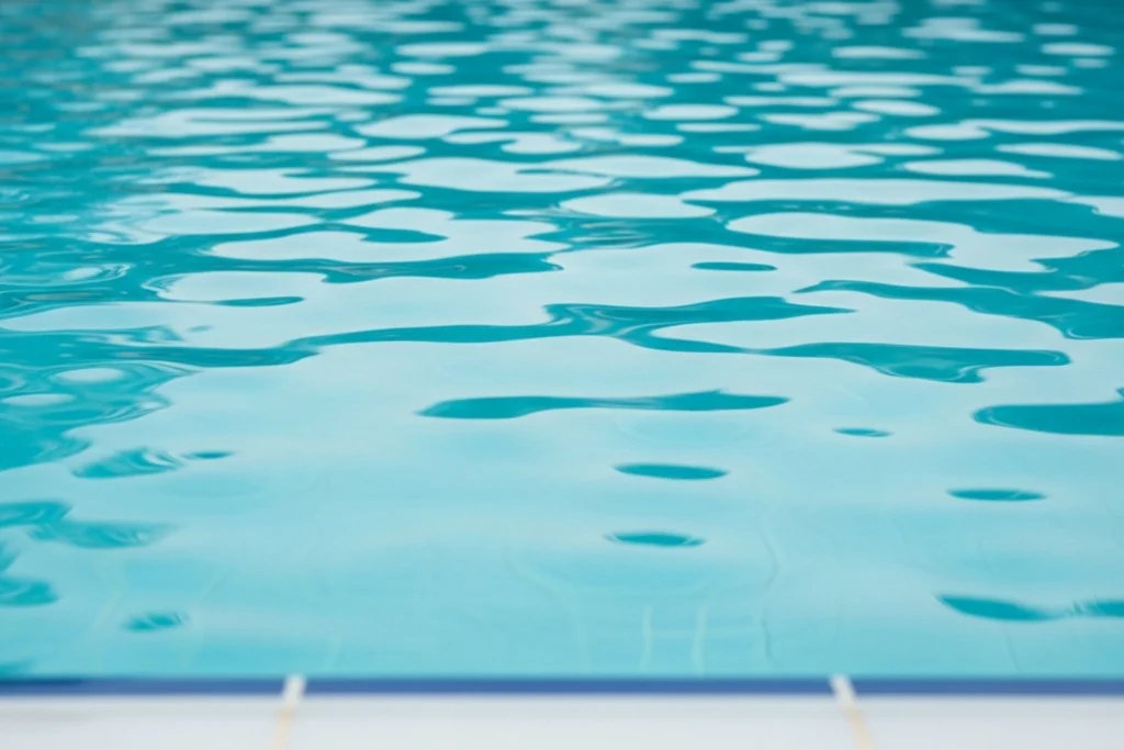 Close-up of calm blue swimming pool water with soft ripples and the pool edge visible in the foreground.