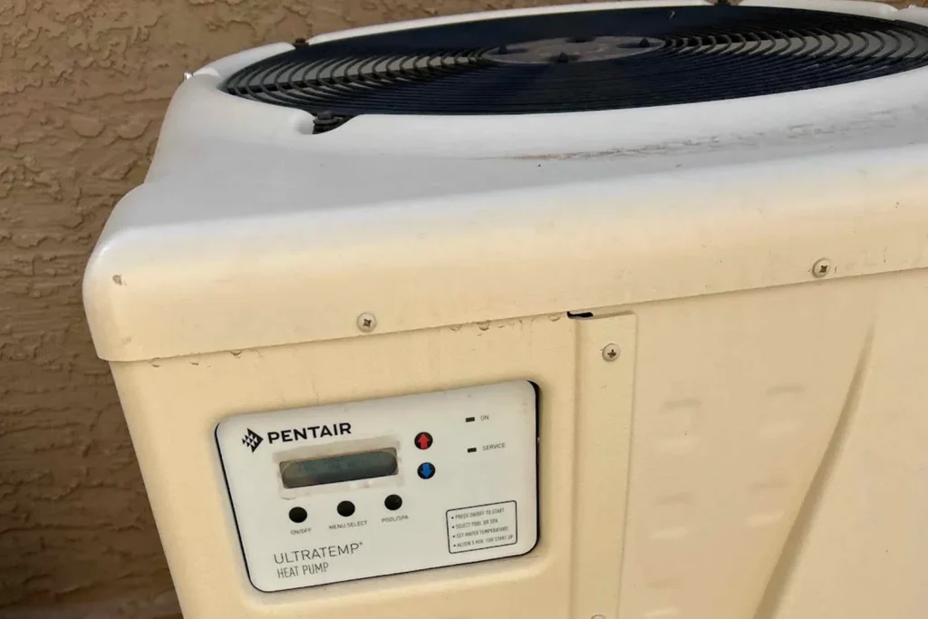 Pentair UltraTemp pool heat pump with built-in control panel and top fan installed on gravel beside an outdoor equipment pad.