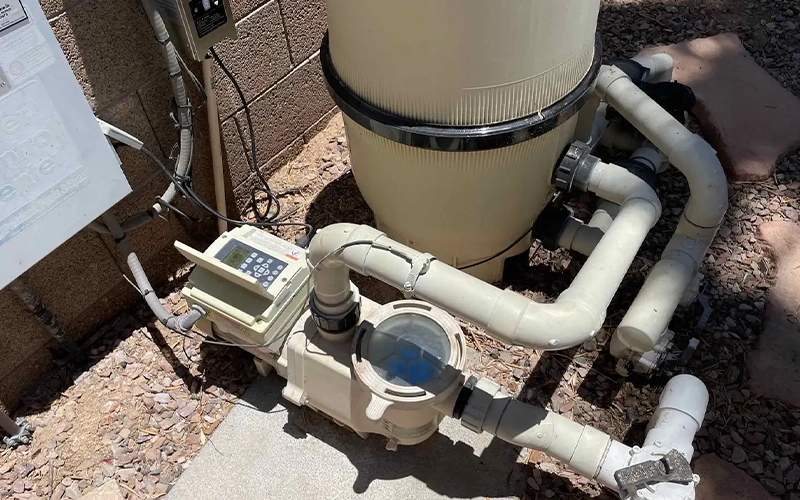 Pool equipment setup with a cartridge filter, pump, timer control box, and PVC plumbing installed on an outdoor equipment pad.