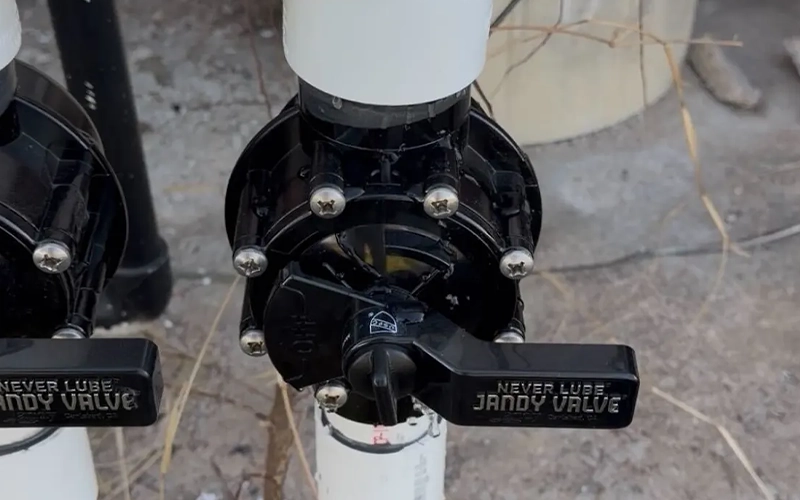 Close-up of a Jandy pool plumbing valve connected to white PVC piping with a 90-degree elbow fitting on an outdoor equipment pad.