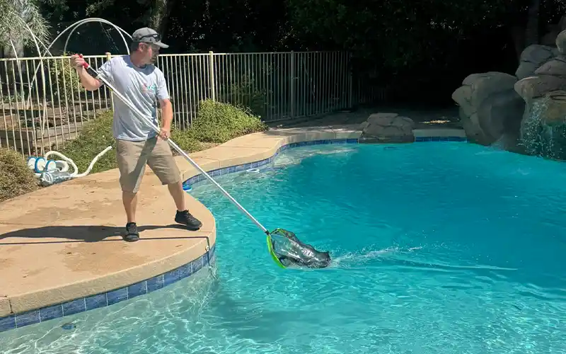 Pool technician skimming a residential swimming pool during a weekly cleaning visit