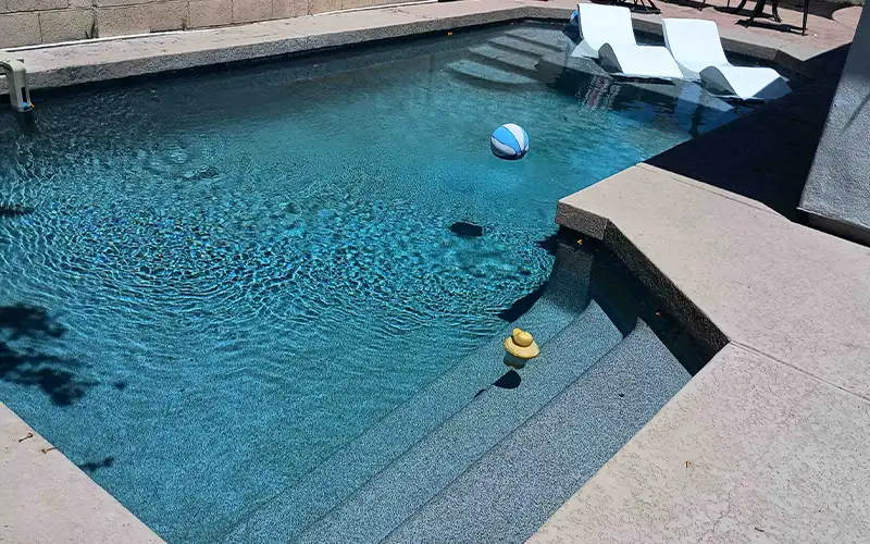 Blue swimming pool with curved entry steps, floating beach ball, and white lounge chairs