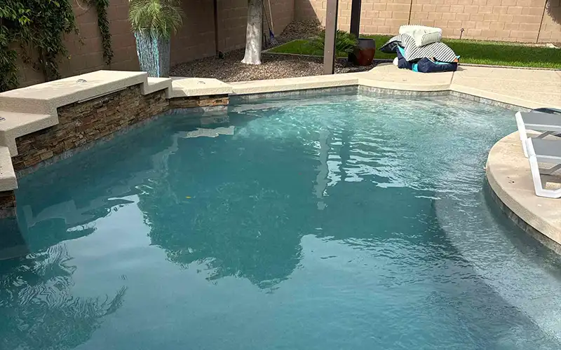 Residential backyard pool with curved edges, stone coping, raised spa area, and surrounding landscaping