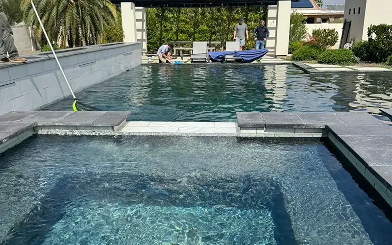 Professional pool technician cleaning a residential pool with clear water during routine pool maintenance service in Arizona