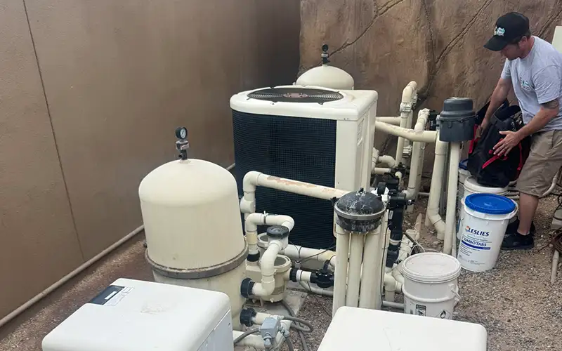 Pool equipment pad with heaters, filters, pumps, PVC plumbing, and a technician inspecting the equipment