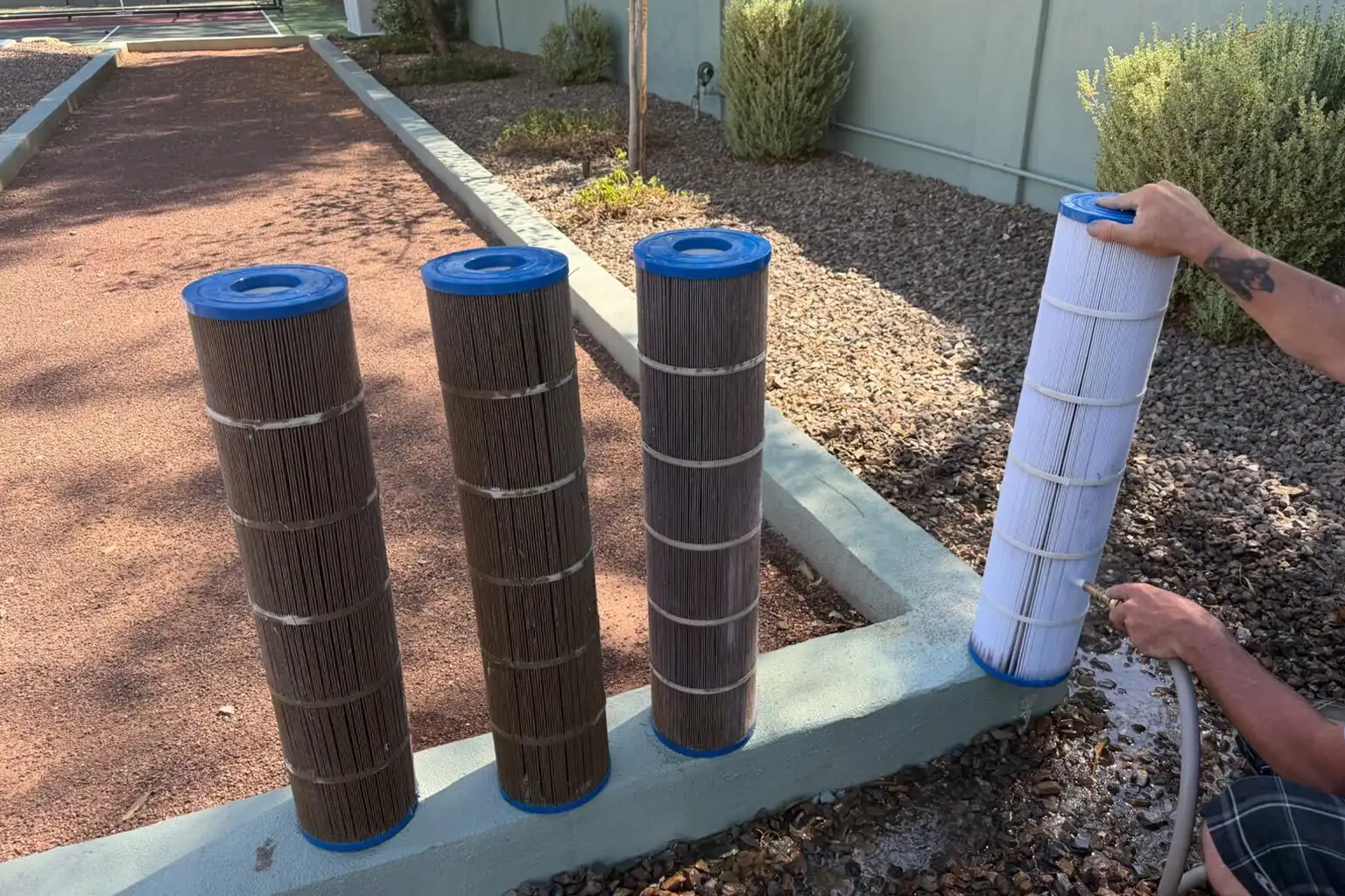 Pool filter cartridges being rinsed with a hose beside a residential pool equipment area