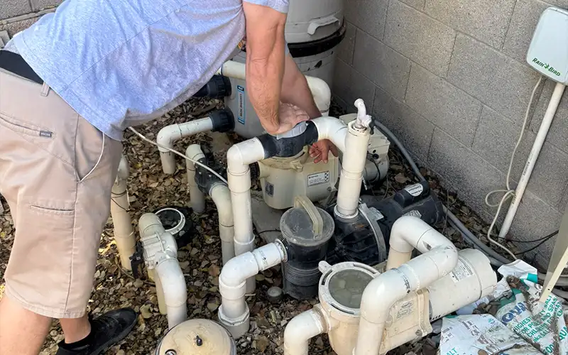 Pool technician inspecting residential pool equipment pad with pumps, filters, plumbing connections, and maintenance components in Scottsdale Mesa Arizona