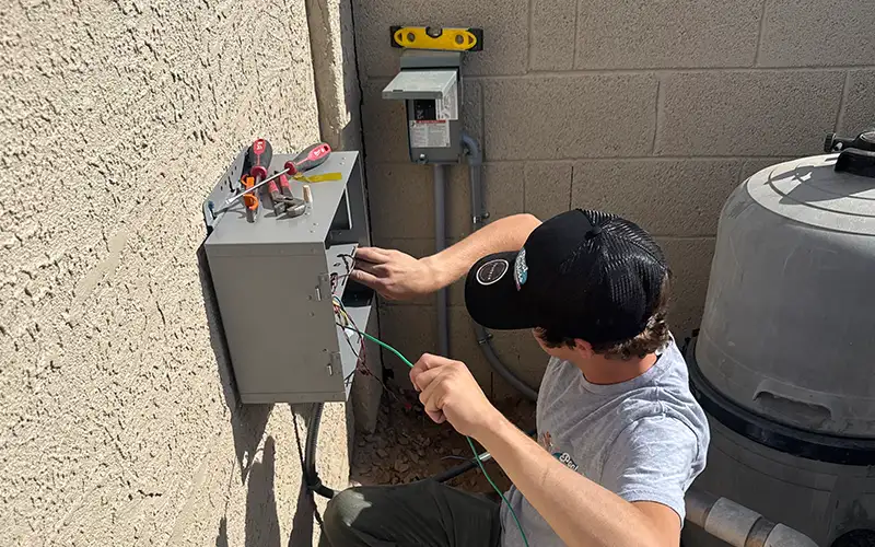 Pool technician working on an electrical control panel beside a pool filtration tank