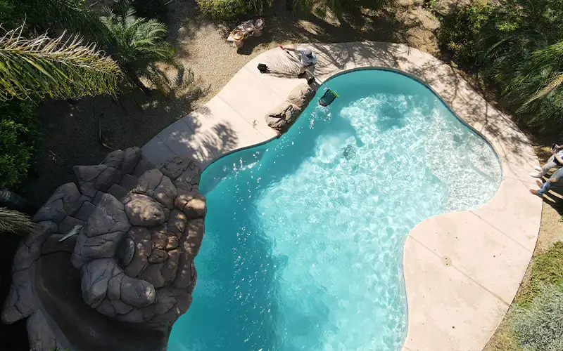 Professional pool technician cleaning a clear residential swimming pool to maintain comfortable water quality